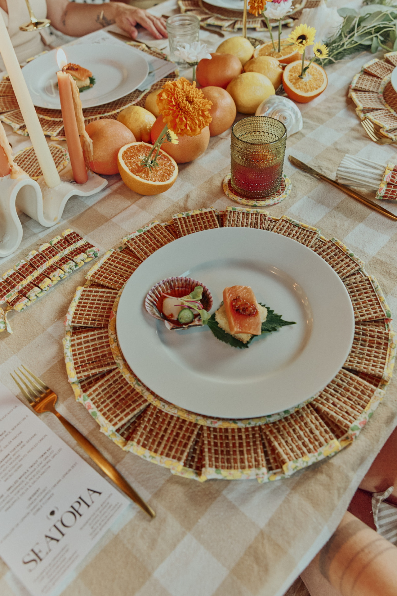 Place setting with woven charger, tapered candles and citrus centerpiece