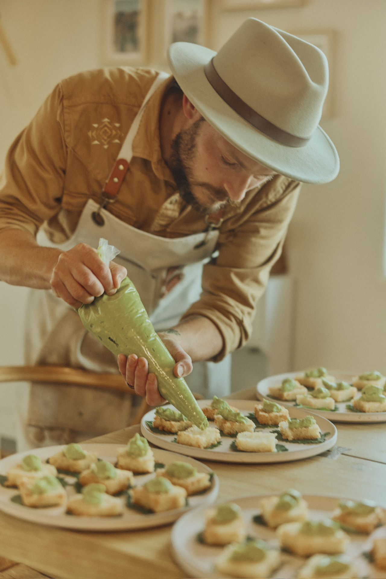 Chef piping avocado mousse onto canapés in a sunlit kitchen