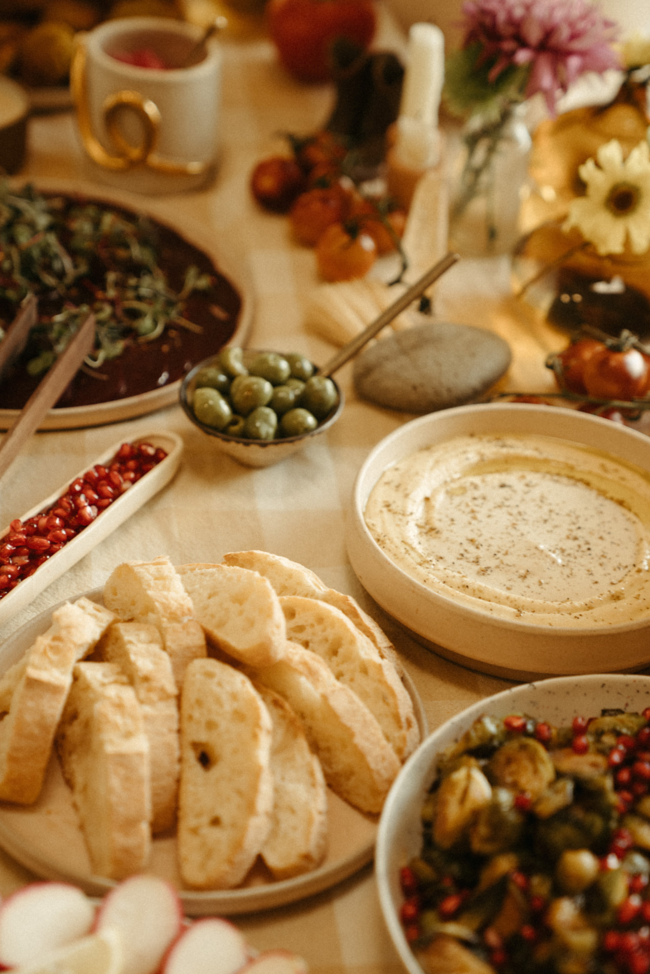 Sliced baguette, hummus, olives and pomegranate on a warm-lit table