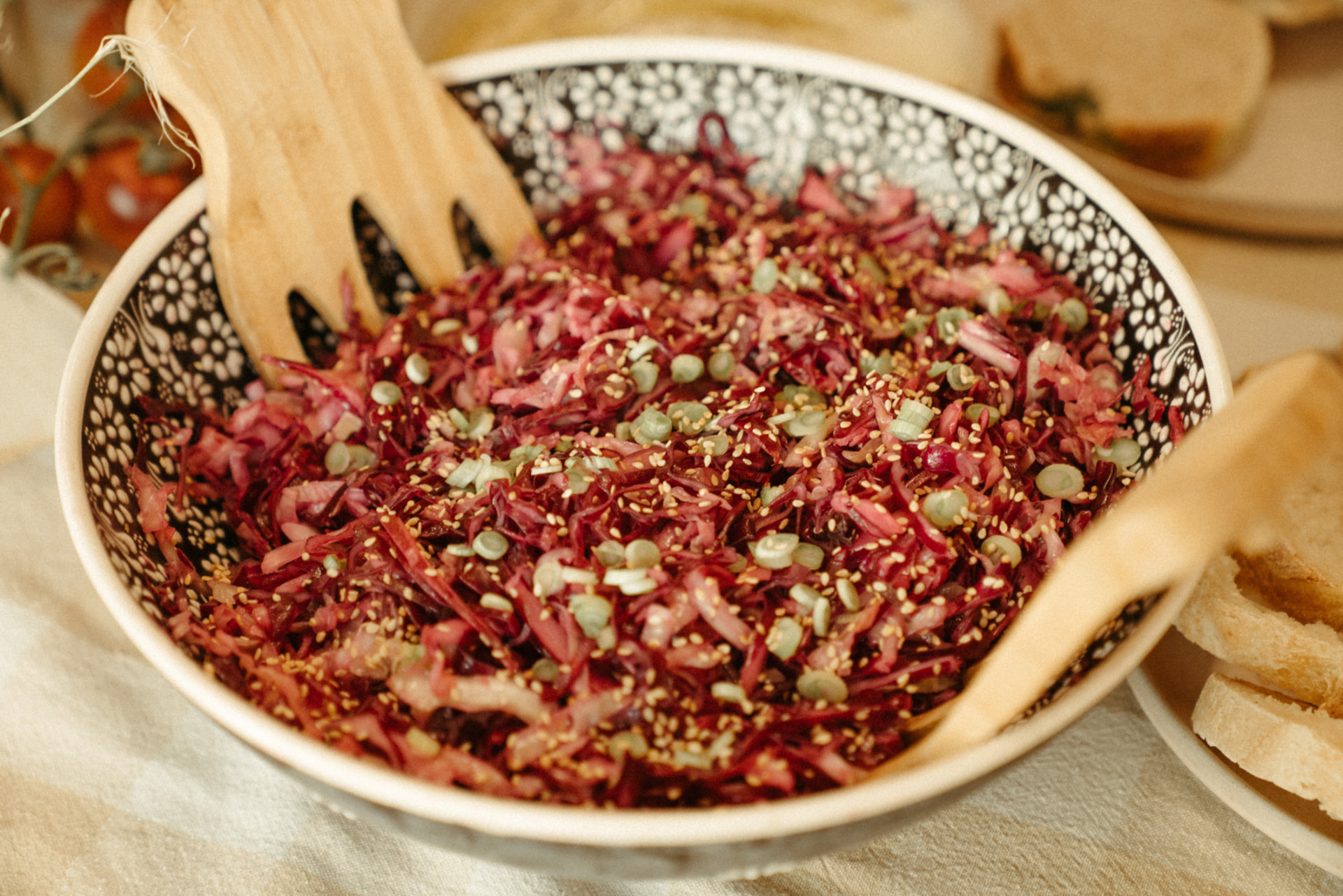 Bowl of shredded beet and cabbage slaw with sesame and scallions beside fresh bread