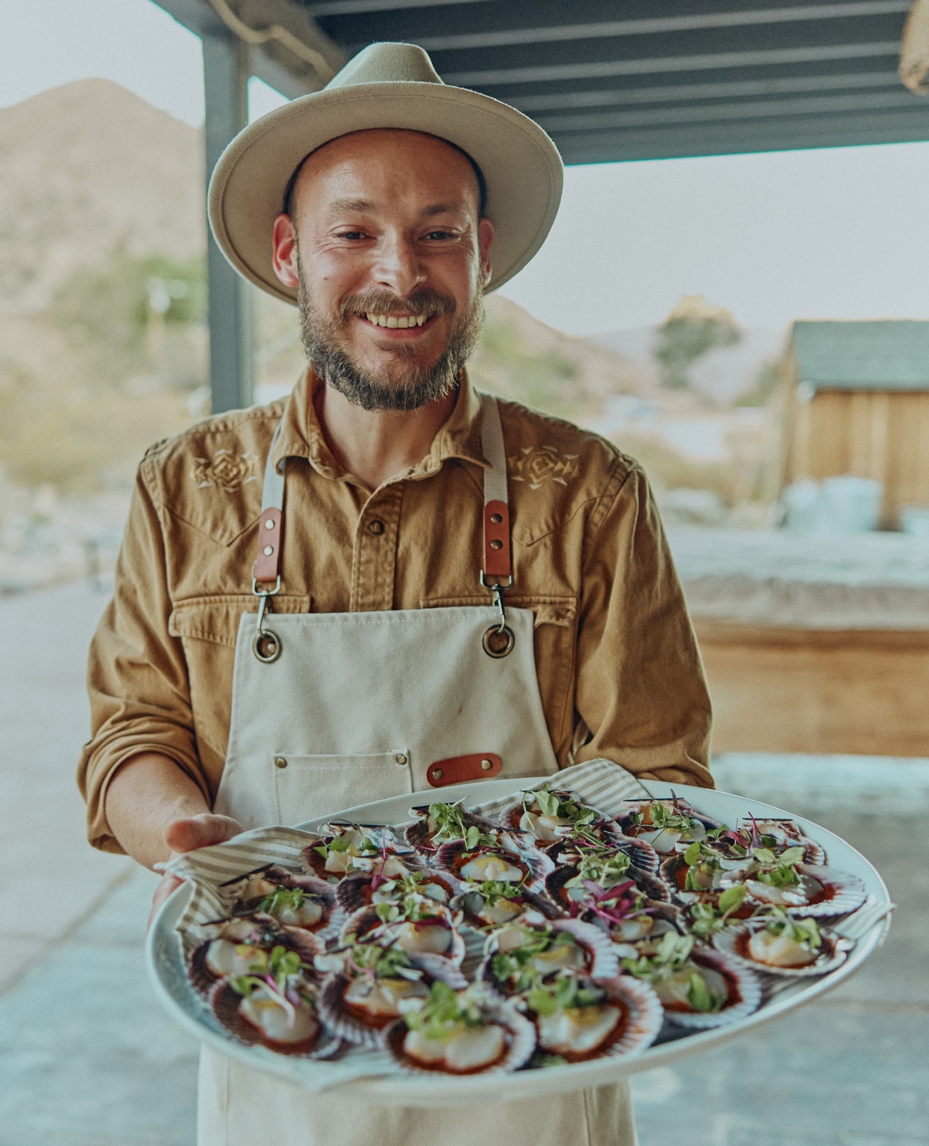 Chef Daniel Ceballos holding a platter of scallop crudo outdoors